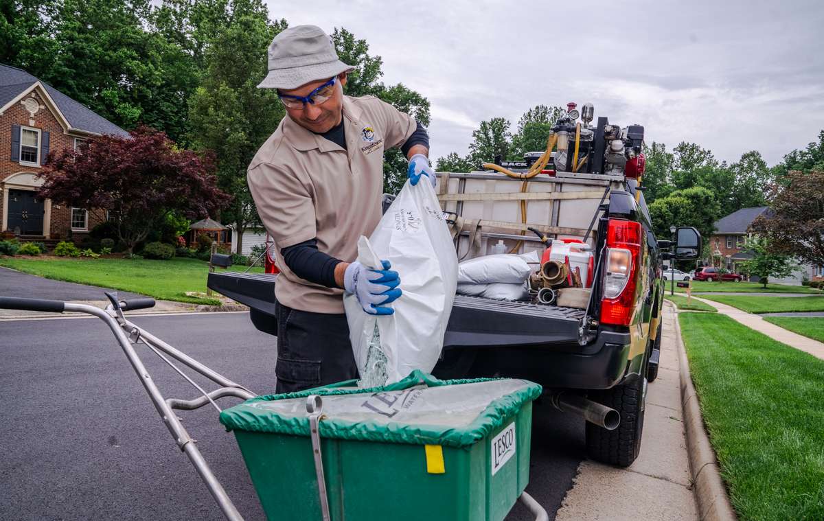 lawn care technician pouring fertilizer into spreader