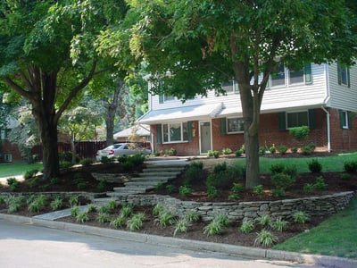 sloped front yard with retaining wall, plants, and trees