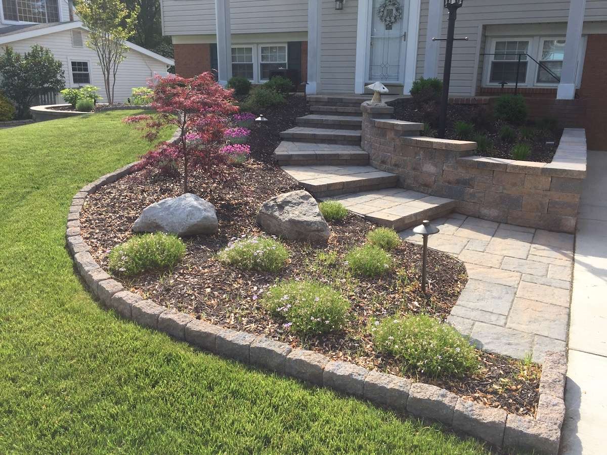 paver walkway with landscape bed full of plantings and weeds
