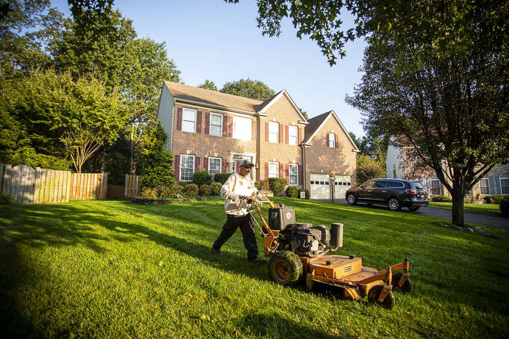 lawn maintenance crew mows lawn with walk behind