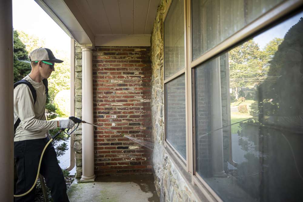 pest control technician spraying exterior of home for pests
