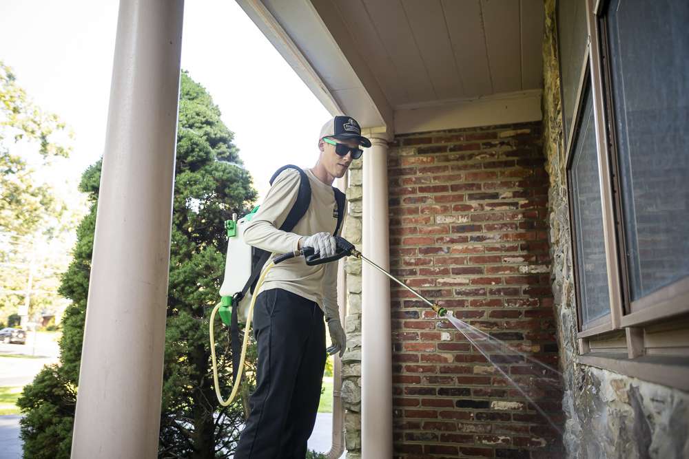 Pest control technician spraying the perimeter of a house