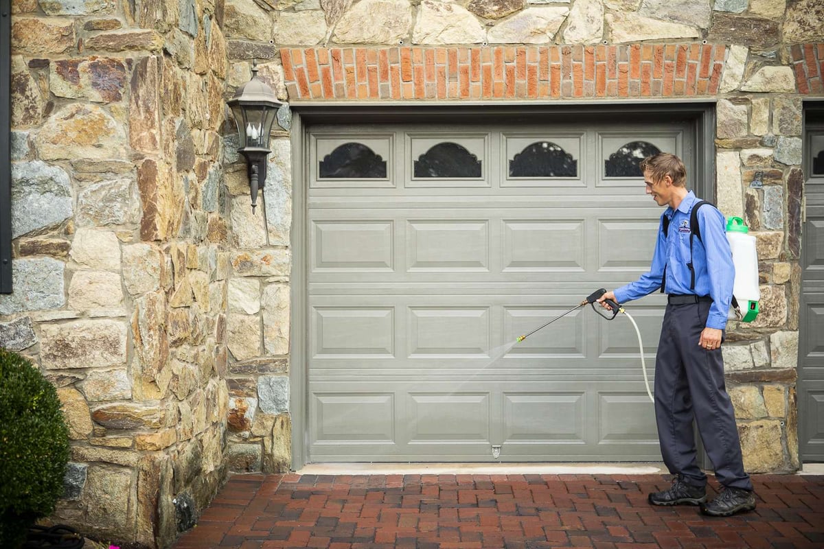 pest control technician spraying exterior of garage