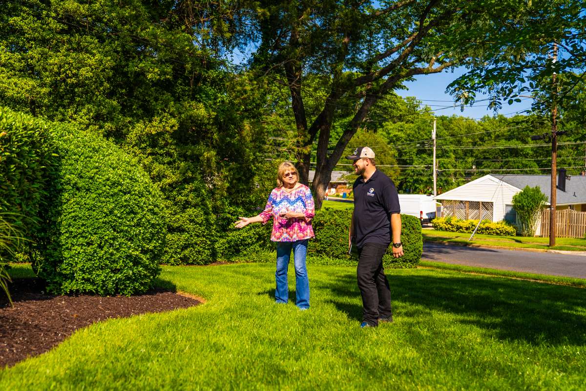 residential landscape maintenance account manager and customer inspecting a planting bed and lawn area