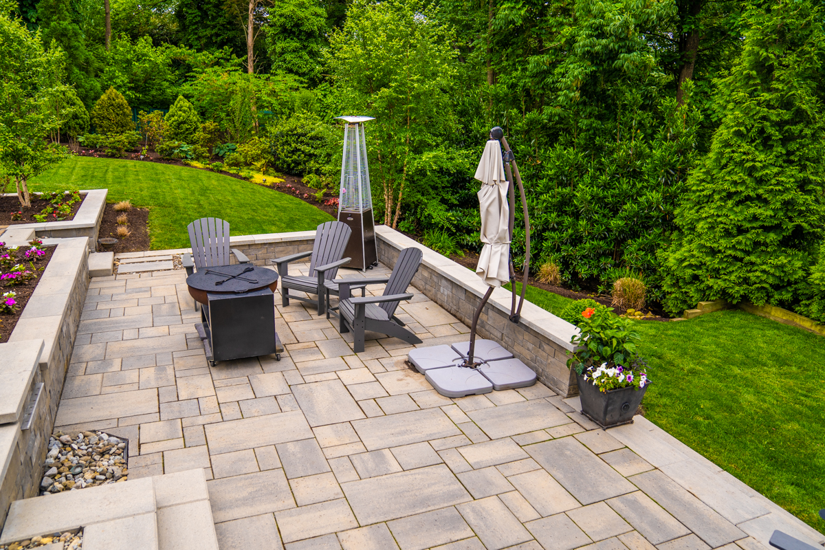 hardscape patio and retaining wall with lawn furniture and border plantings on a sloped backyard