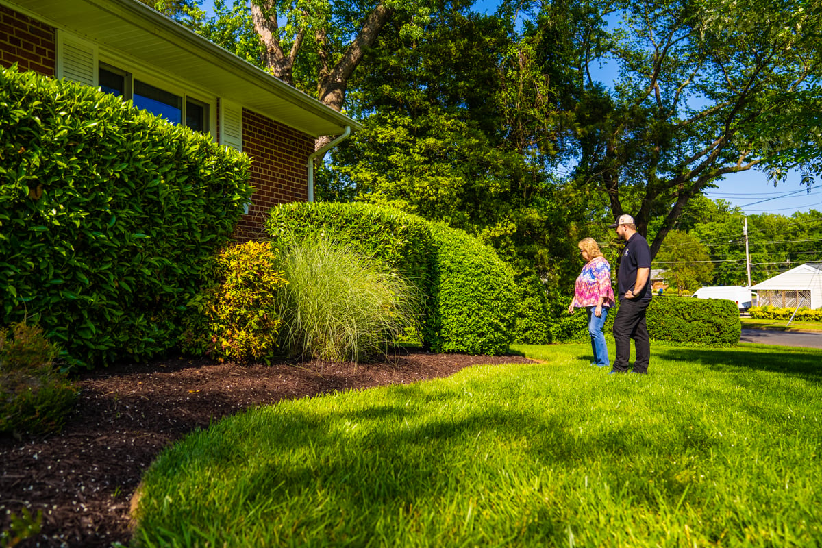 residential landscape maintenance account manager and customer inspecting a planting bed and lawn area