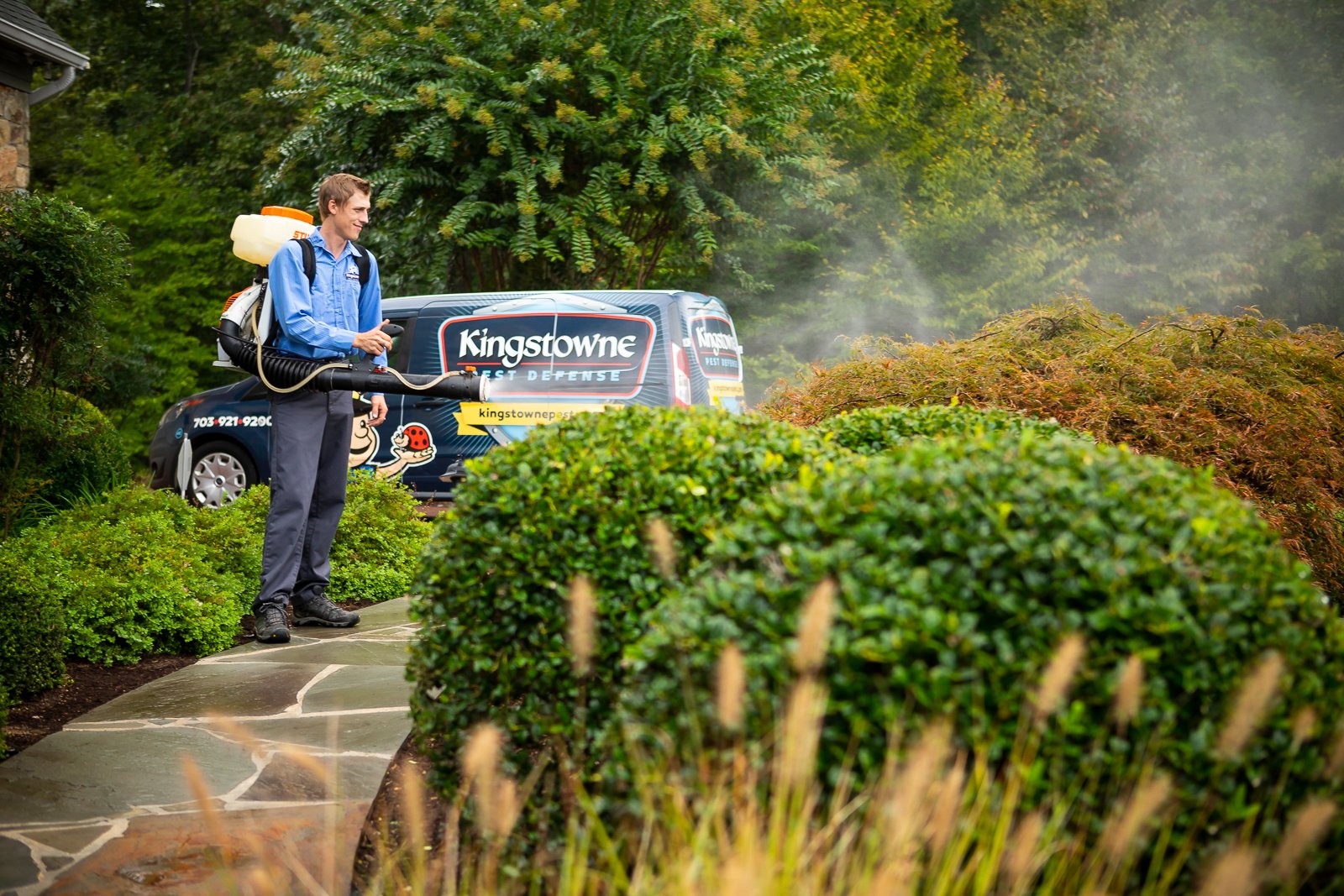 mosquito control technician applying mosquito barrier spray to a landscape planting bed